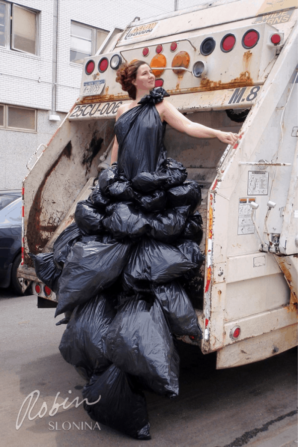 a woman stand on a garbage vehicle wearing a dress made up by trash bag